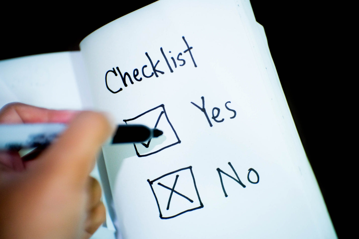 Hand marking a checklist with options 'Yes' and 'No' written on a notepad.