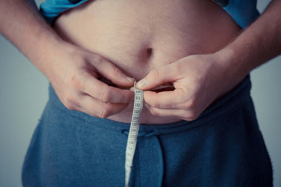 Man measuring his waist with a tape measure, focusing on love handles and abdominal area.