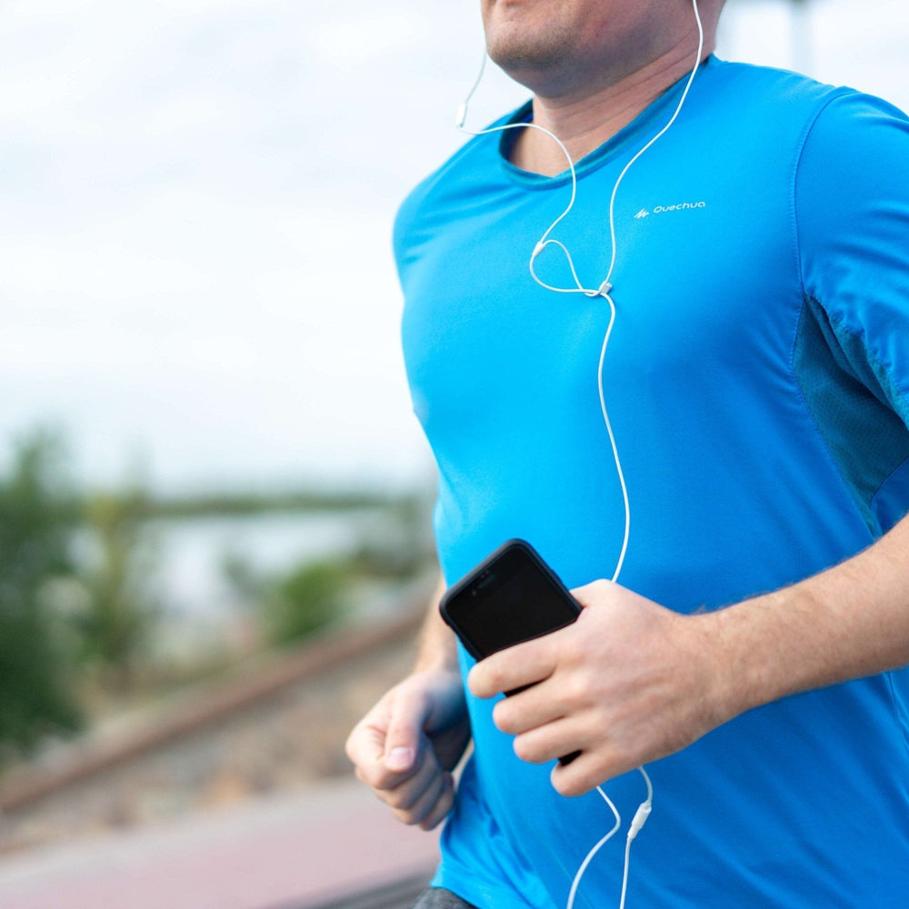 Man running outdoors in a blue athletic shirt, listening to music with earbuds and holding a smartphone.